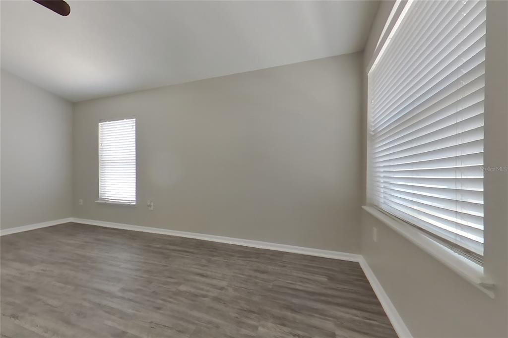 An empty room features light gray walls, wood-look flooring, and two windows with white blinds — 353 COMFORT DRIVE, APOPKA, FL