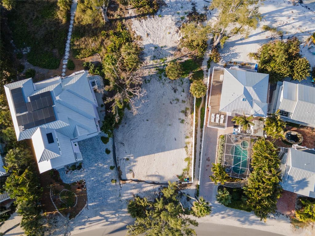 An aerial view shows a vacant sandy lot situated between two houses with metal roofs — 831 NORTH SHORE DRIVE, ANNA MARIA, FL