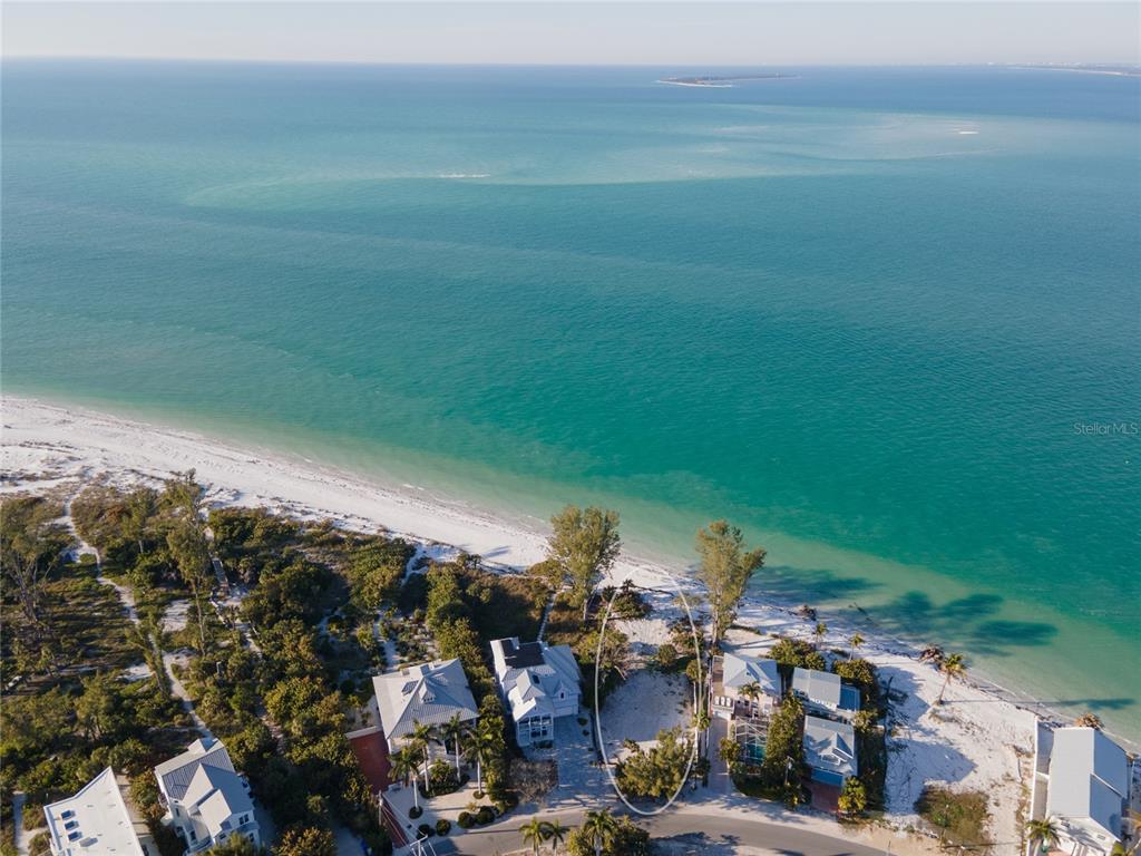 An aerial view shows a vacant beachfront lot situated between two houses along the coast — 831 NORTH SHORE DRIVE, ANNA MARIA, FL