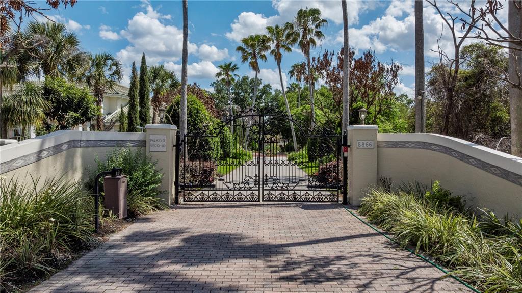 A paved driveway leads to an ornate black metal gate flanked by stucco walls — 8866 DARLENE DRIVE, ORLANDO, FL