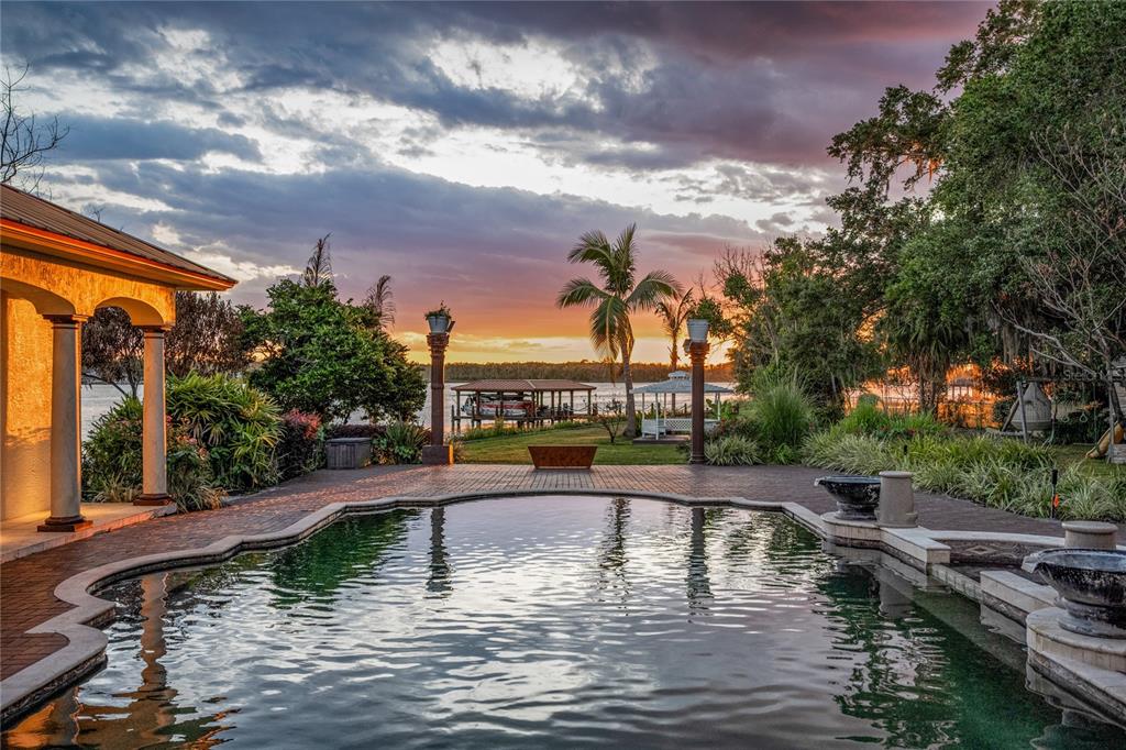 A swimming pool overlooks a lake at sunset with a boat dock and palm trees — 8866 DARLENE DRIVE, ORLANDO, FL