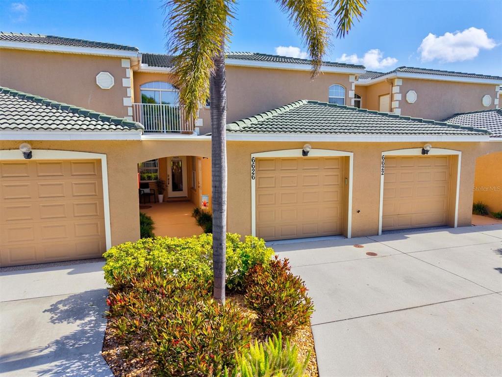A multi-unit residential building exterior features tan stucco walls, green tile roofs, and three garages — 6626 7TH AVENUE CIRCLE W, BRADENTON, FL
