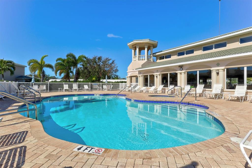 A swimming pool with a brick deck sits in front of a multi-story building — 6626 7TH AVENUE CIRCLE W, BRADENTON, FL