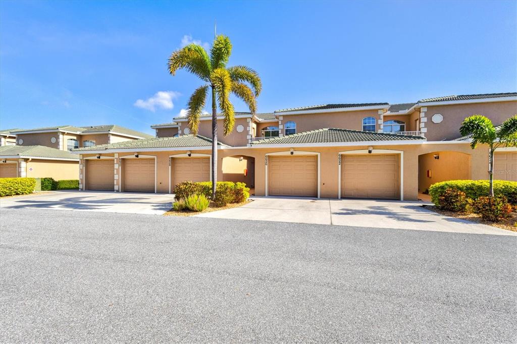 A row of tan townhouses features multiple garage doors and a palm tree in front — 6626 7TH AVENUE CIRCLE W, BRADENTON, FL