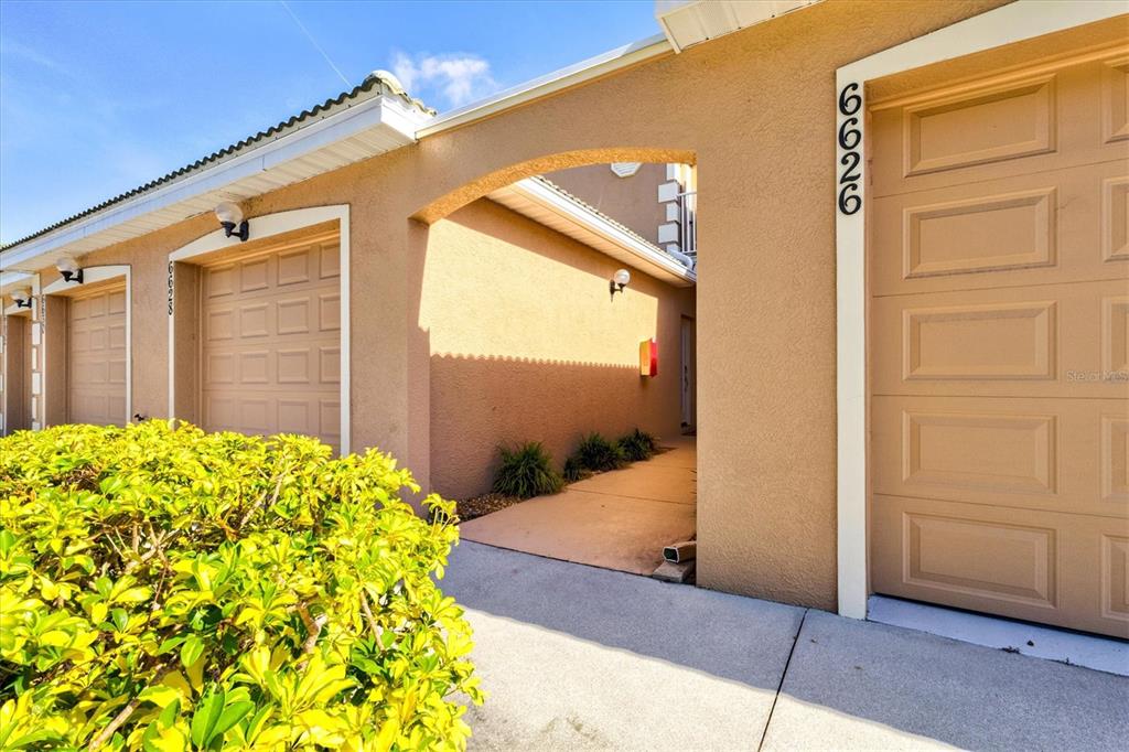 A beige stucco exterior features two garage doors and a covered walkway between them — 6626 7TH AVENUE CIRCLE W, BRADENTON, FL
