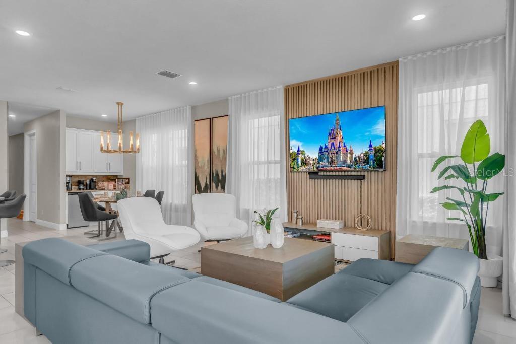 A modern living room features a blue sectional sofa, wood slat wall, and dining area — 1117 CASTLE PINES COURT, REUNION, FL