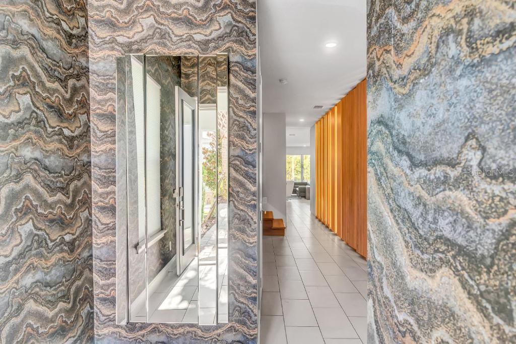 A hallway features patterned wallpaper, a mirrored accent wall, and a wood-slatted feature wall — 1117 CASTLE PINES COURT, REUNION, FL
