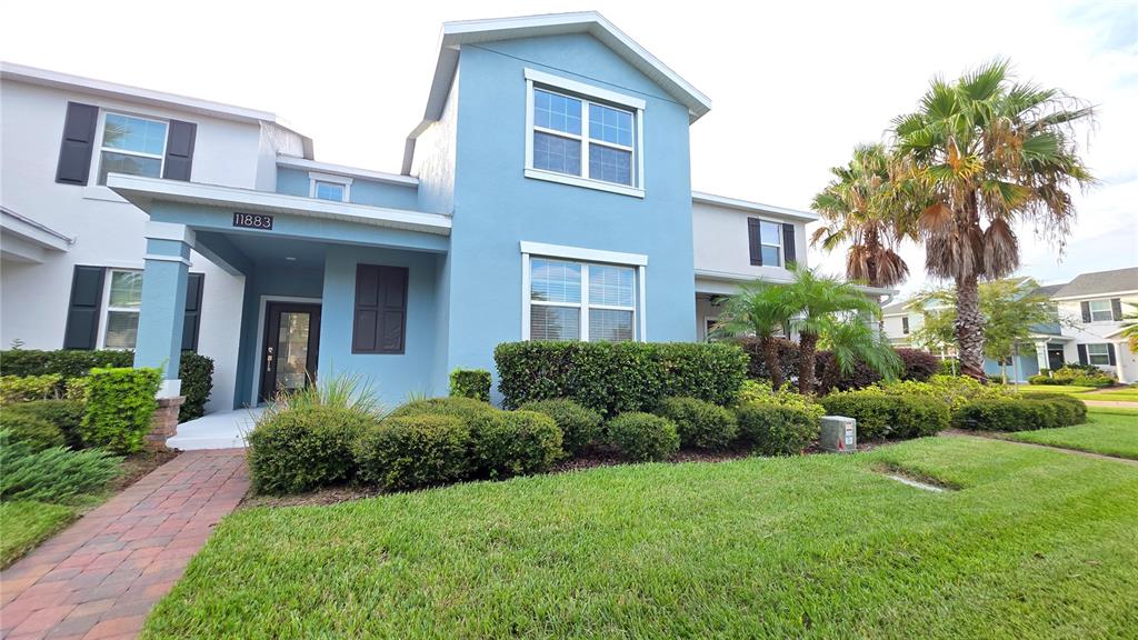 A two-story blue house features a covered entryway, a brick walkway, and landscaped front bushes — 11883 PULITZER PLACE, ORLANDO, FL
