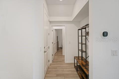 A hallway with light wood-look flooring leads to a doorway, featuring a metal shelving unit — 2099 DERWENT DRIVE, DAVENPORT, FL