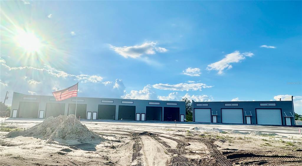 A row of newly constructed commercial warehouse units with roll-up doors under a bright sky — 4017 TAYLOR ROAD UNIT D3or 6, PUNTA GORDA, FL