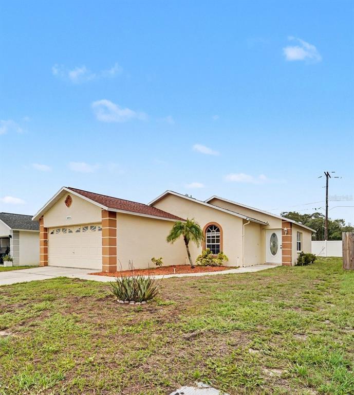 A single-story house with a beige stucco exterior, a two-car garage, and a front lawn — 10236 FLAGSHIP AVENUE, PORT RICHEY, FL