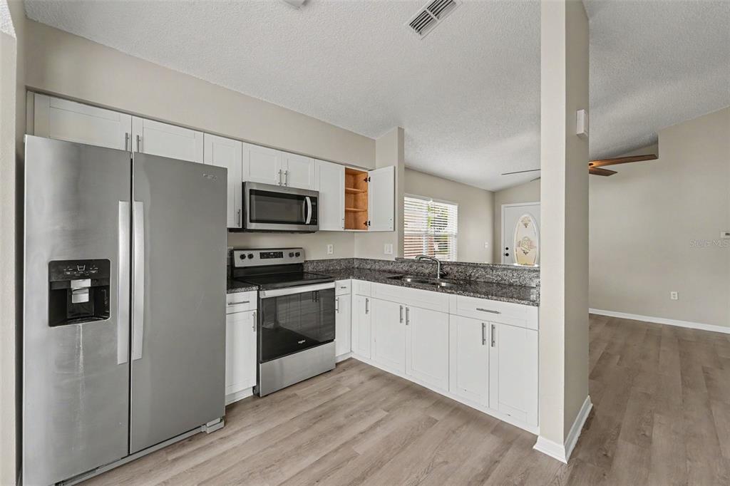 A kitchen with white cabinets, stainless steel appliances, and granite countertops opens to a living area — 10236 FLAGSHIP AVENUE, PORT RICHEY, FL