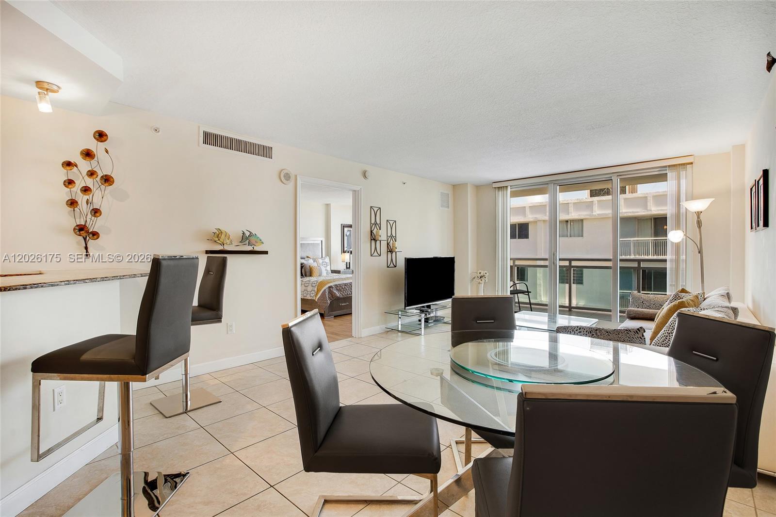 A dining and living area features a glass table, bar stools, and a balcony view — 6917 Collins Ave # 1608, Miami Beach FL 33141, MIAMI BEACH, FL