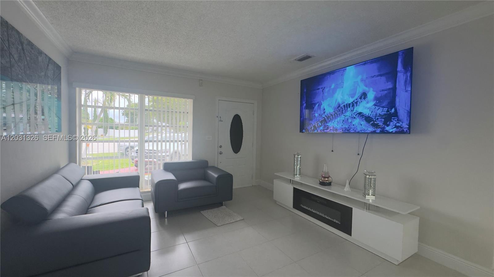 A living room features a grey sofa, matching armchair, white media console, and wall-mounted television — 12480 SW 189th St, Miami FL 33177, MIAMI, FL