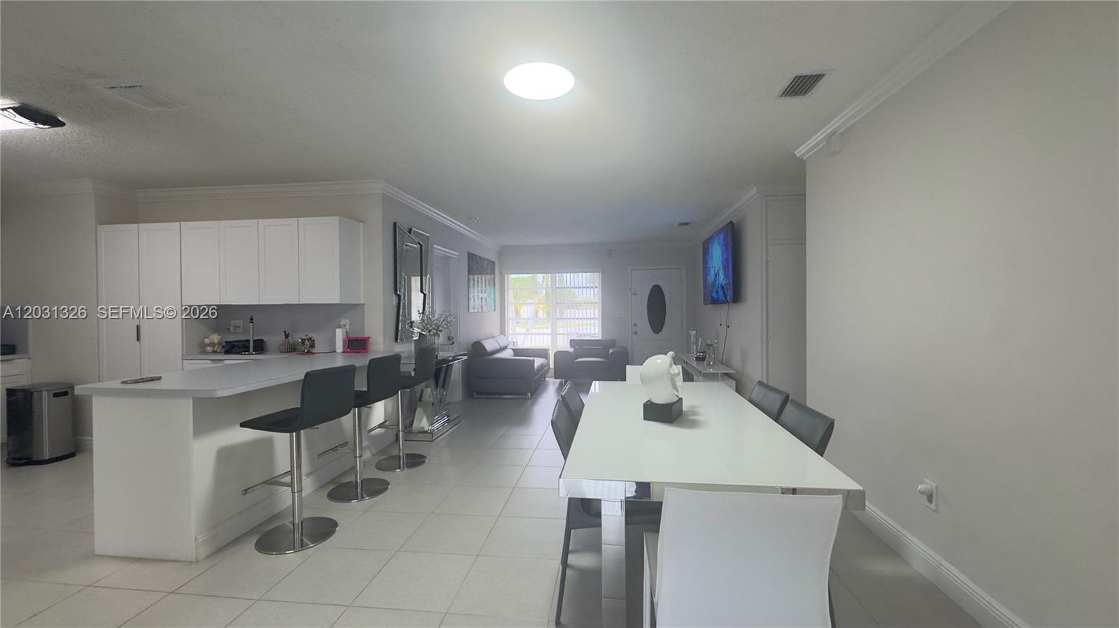 This open-concept living area features a white kitchen, a dining table, and tile flooring — 12480 SW 189th St, Miami FL 33177, MIAMI, FL