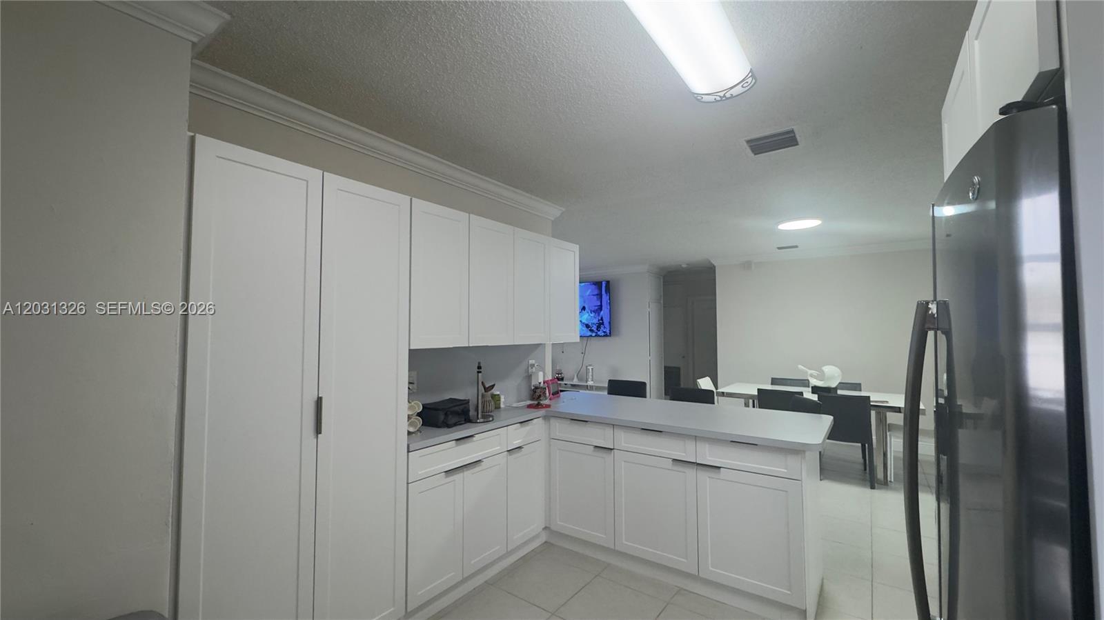 A kitchen features white cabinetry, gray countertops, and a breakfast bar overlooking a dining area — 12480 SW 189th St, Miami FL 33177, MIAMI, FL