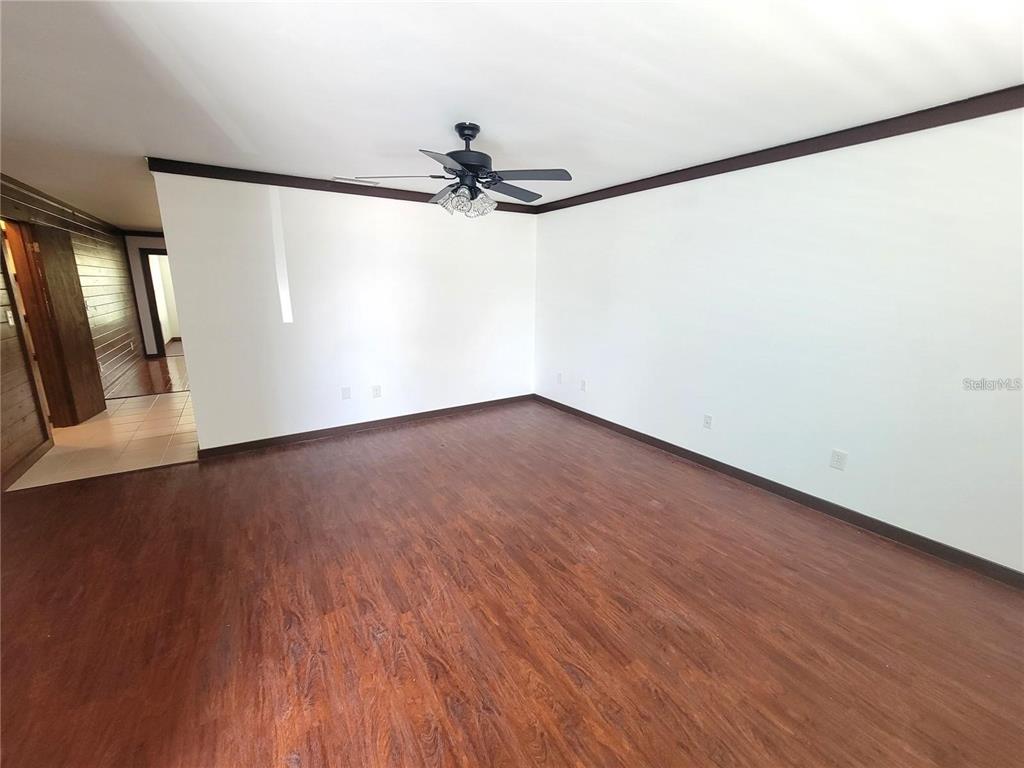 An empty room features wood-look flooring, white walls, dark crown molding, and a ceiling fan — 306 63RD STREET UNIT B, HOLMES BEACH, FL