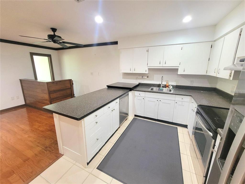 A kitchen with white cabinets, dark countertops, and a tile floor overlooks a wood-floored area — 306 63RD STREET UNIT B, HOLMES BEACH, FL