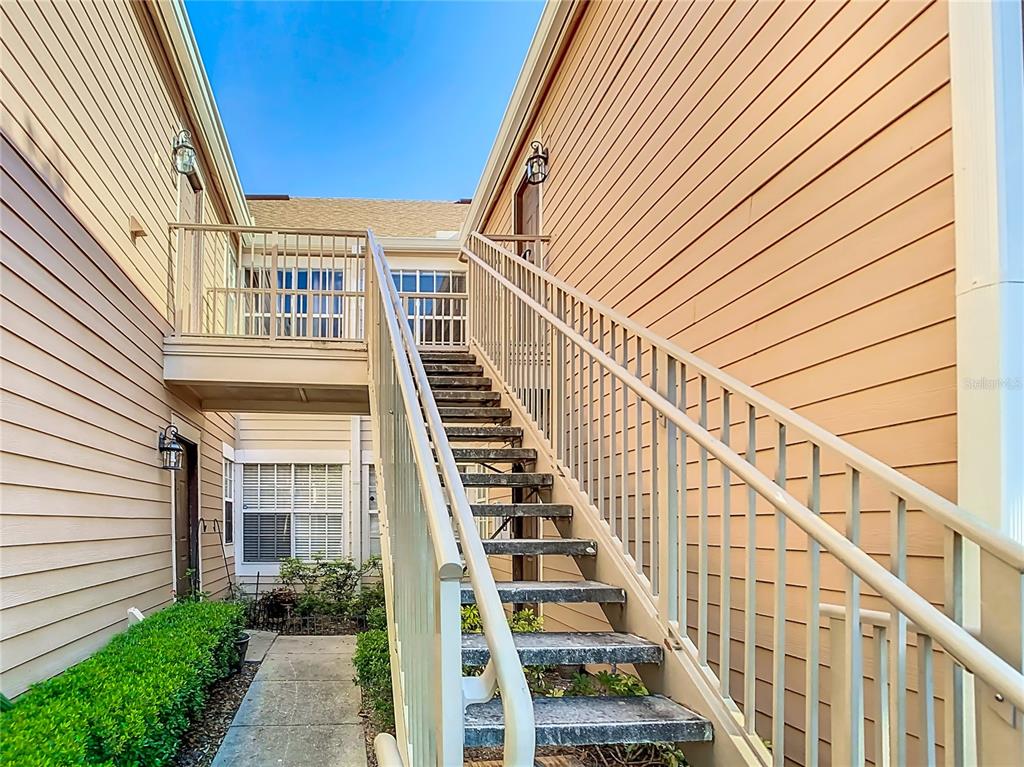 An exterior view of a tan building featuring a metal staircase leading to an upper walkway — 665 YOUNGSTOWN PARKWAY UNIT 262, ALTAMONTE SPRINGS, FL