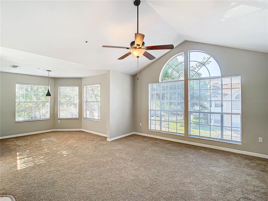 A spacious living room features beige carpeting, a vaulted ceiling with a fan, and large windows — 665 YOUNGSTOWN PARKWAY UNIT 262, ALTAMONTE SPRINGS, FL