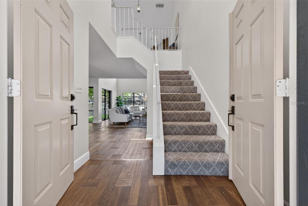 An entryway features a carpeted staircase, white walls, and wood flooring leading to a living area — 713 CAYA COSTA COURT NE, ST PETERSBURG, FL