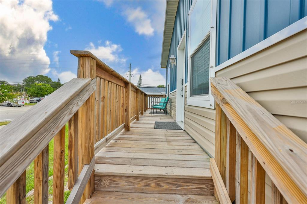 A wooden deck with railings leads to the entrance of a blue and beige home — 1169 8TH AVENUE NE, LARGO, FL