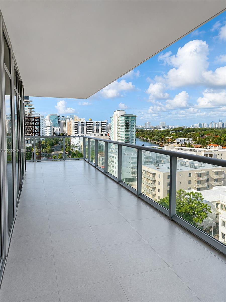 A spacious balcony with light-colored tile flooring and a glass railing overlooks a city skyline — 3737 Collins Ave # 1003, Miami Beach FL 33140, MIAMI BEACH, FL