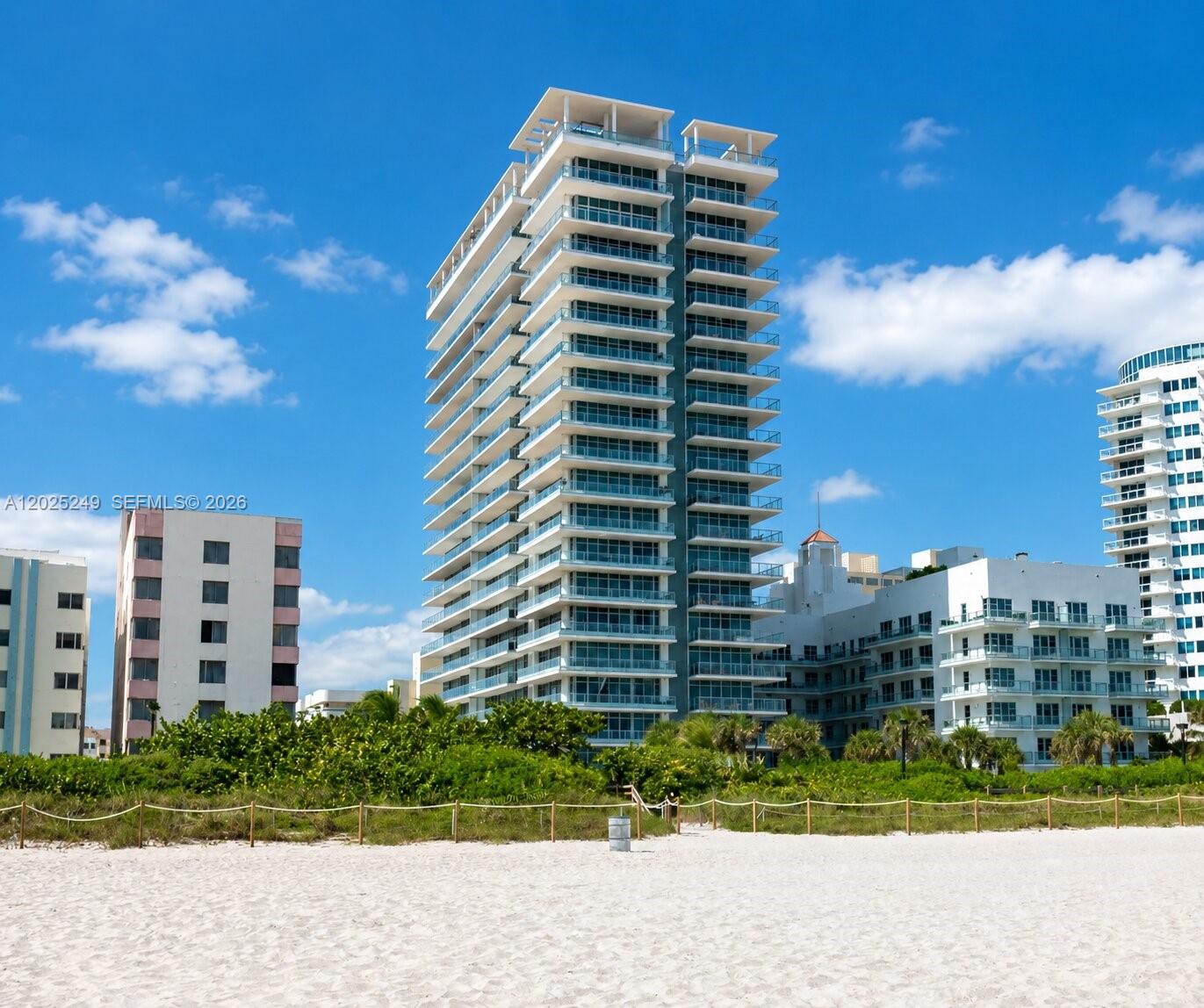 A tall, modern residential building stands behind a sandy beach under a blue sky — 3737 Collins Ave # 1003, Miami Beach FL 33140, MIAMI BEACH, FL