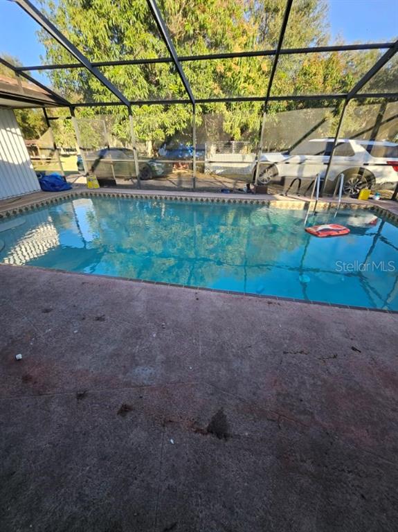 A swimming pool enclosed by a screened lanai with a concrete patio and parked cars — 1826 NW COUNTY ROAD 661, ARCADIA, FL