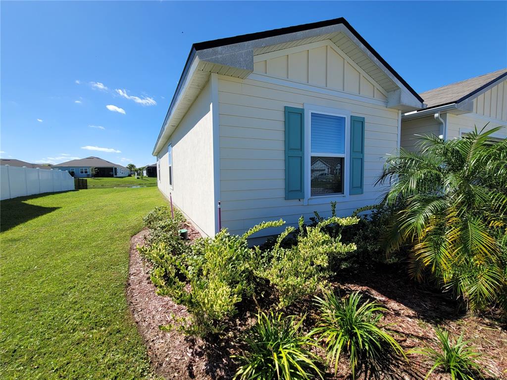 The exterior side of a light-colored house features blue shutters and a landscaped garden bed — 127 HULETT WOODS ROAD, PALM COAST, FL