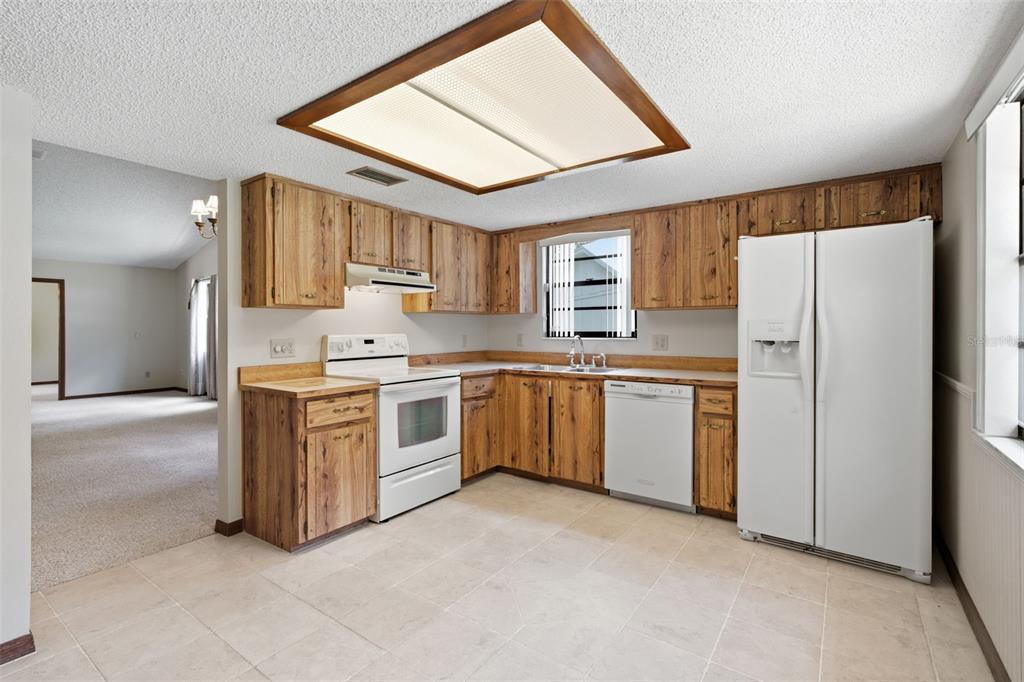 A kitchen features wood cabinets, white appliances, tile flooring, and a large rectangular ceiling light — 30 RAMBLEWOOD TRAIL, DELAND, FL