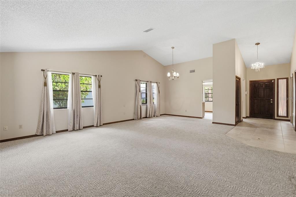 A spacious living room features vaulted ceilings, beige carpeting, and a tiled entryway — 30 RAMBLEWOOD TRAIL, DELAND, FL