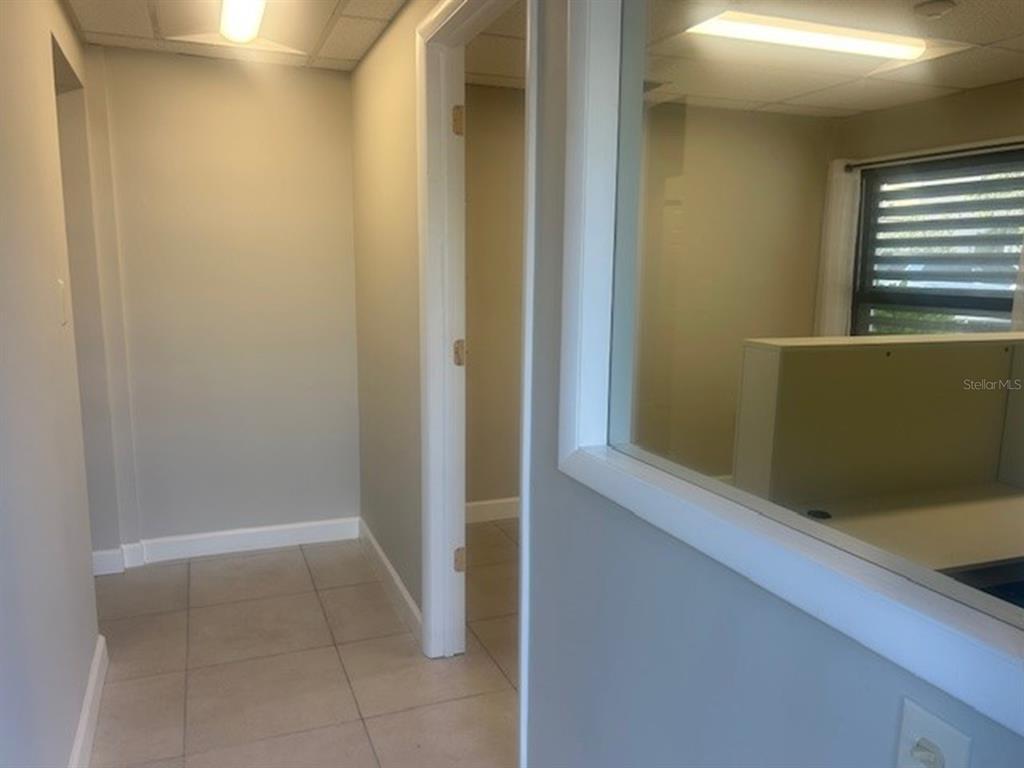 A hallway with tile flooring leads to an office space visible through a glass partition — 2063 MAIN STREET UNIT 102, SARASOTA, FL