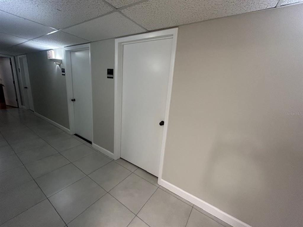 A hallway with light gray walls, white doors, and light-colored tile flooring — 2063 MAIN STREET UNIT 102, SARASOTA, FL
