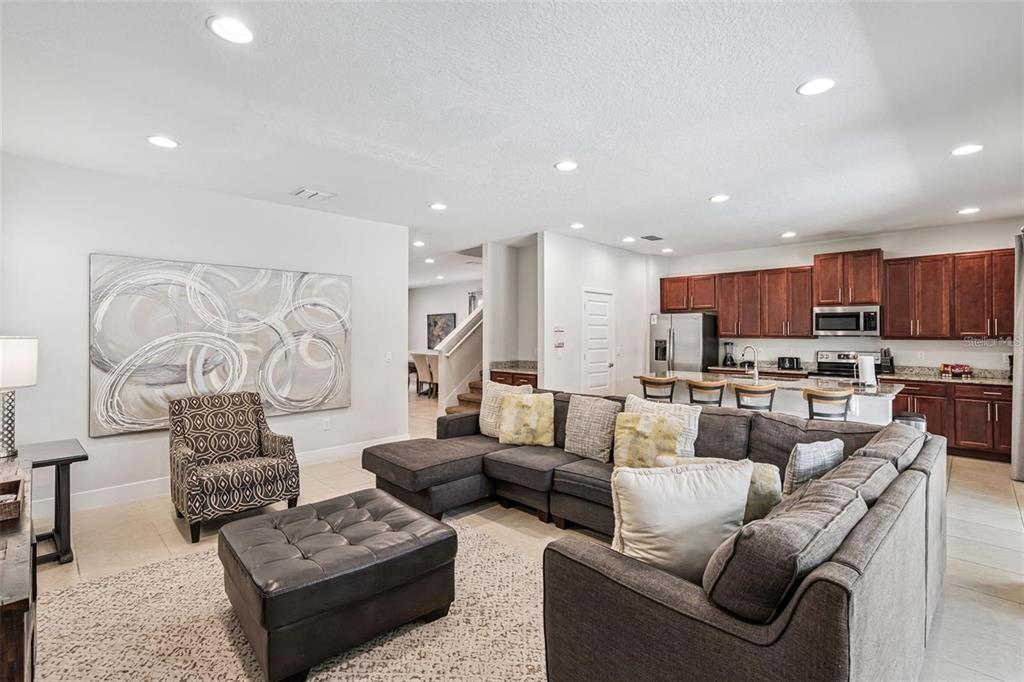 A living room with a sectional sofa, ottoman, patterned armchair, and an open-concept kitchen — 310 PENDANT COURT, KISSIMMEE, FL