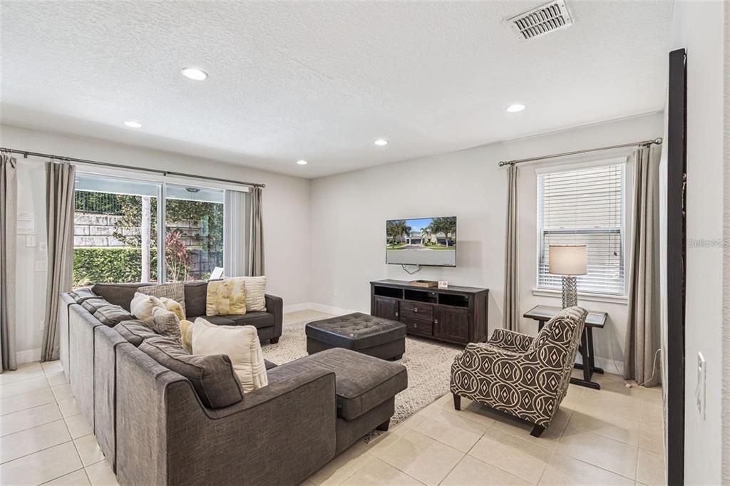 A living room with a gray sectional sofa, patterned armchair, and wall-mounted television — 310 PENDANT COURT, KISSIMMEE, FL