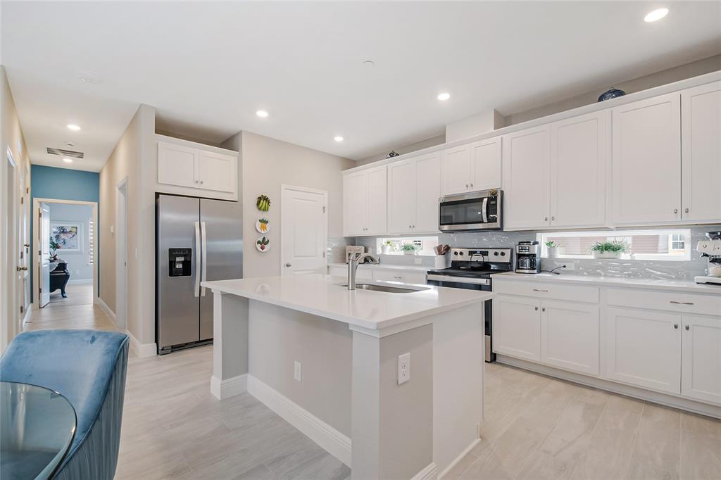 A modern kitchen features white cabinets, stainless steel appliances, a quartz island, and tile flooring — 10009 PEARSON AVENUE, ORLANDO, FL