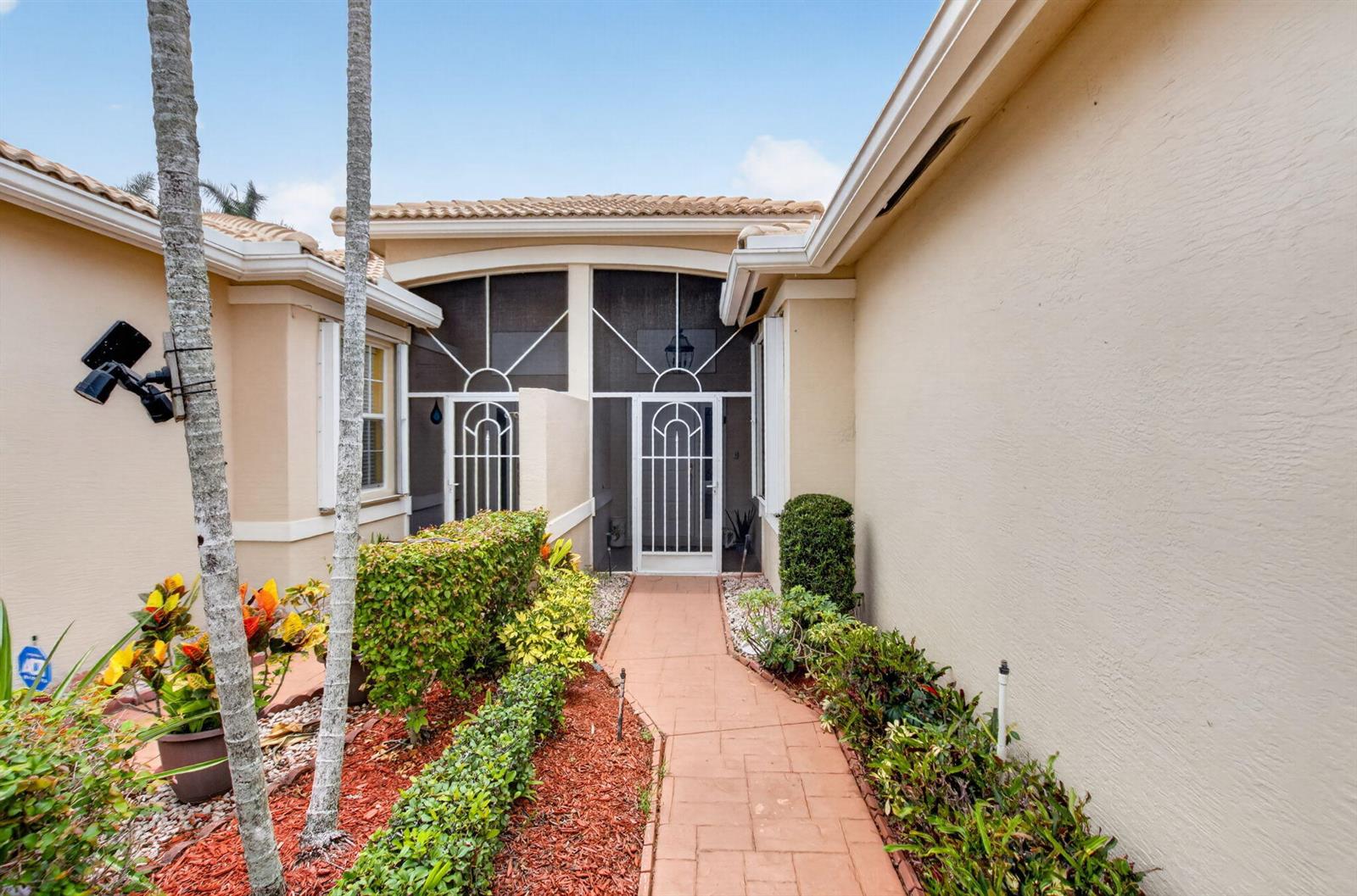 A paved walkway leads to the screened front entryway of a beige stucco house — 10632 Royal Caribbean Circle, Boynton Beach FL 33437, BOYNTON BEACH, FL