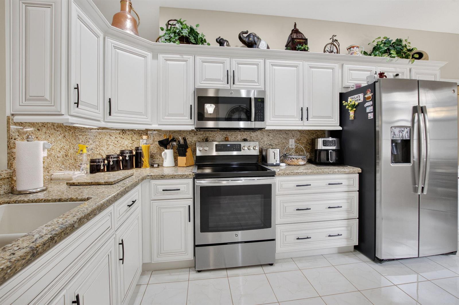 A kitchen features white cabinets, granite countertops, stainless steel appliances, and light-colored tile flooring — 10632 Royal Caribbean Circle, Boynton Beach FL 33437, BOYNTON BEACH, FL