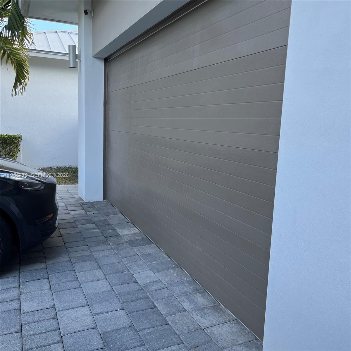 A modern garage door with horizontal panels is set between white walls above a paver driveway — 15062 SW 177th Ter, Miami FL 33187, MIAMI, FL