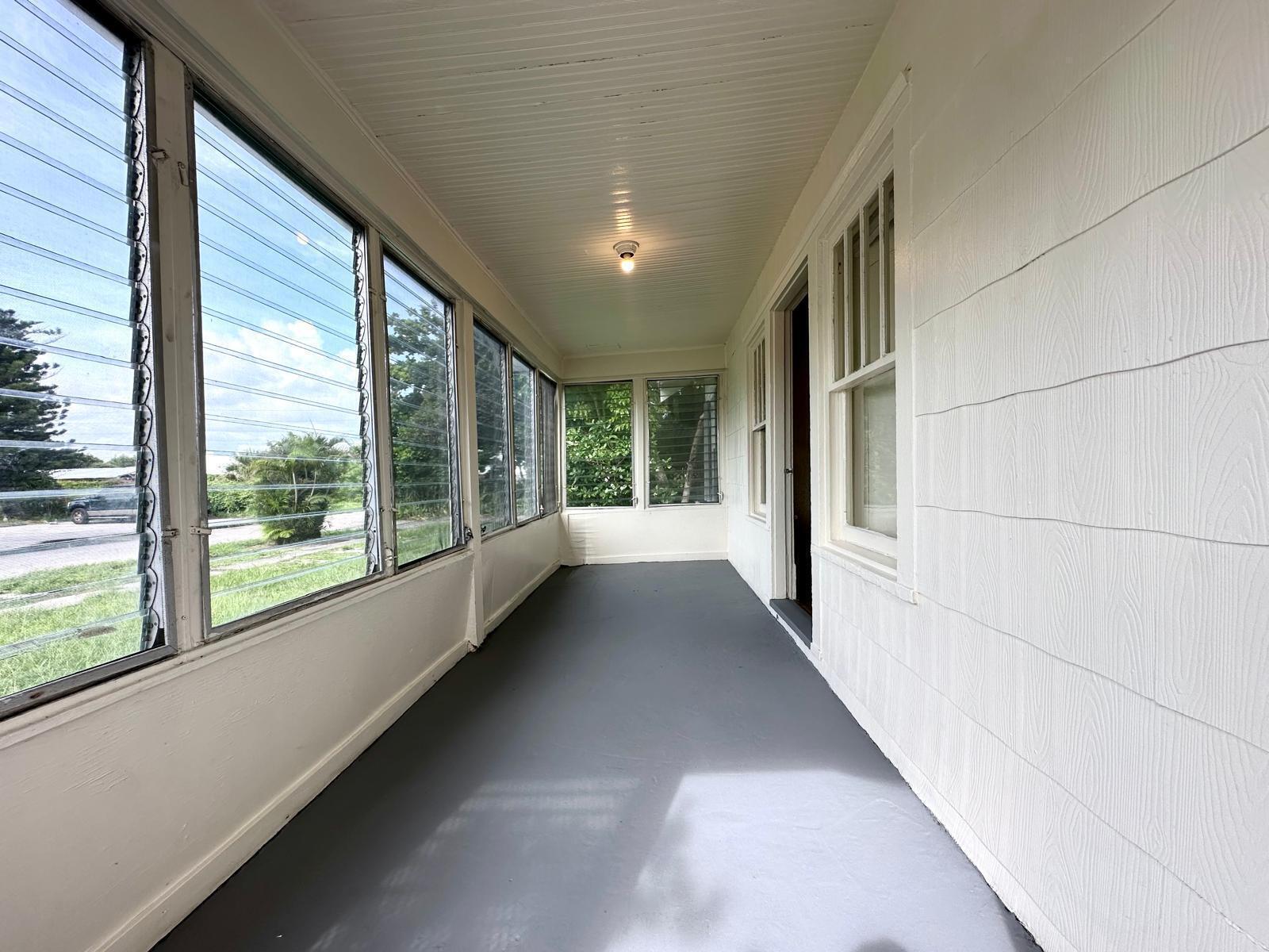 A long, enclosed porch features gray painted flooring, white walls, and multiple louvered glass windows — 523 Valley Forge Road, West Palm Beach FL 33405, WEST PALM BEACH, FL