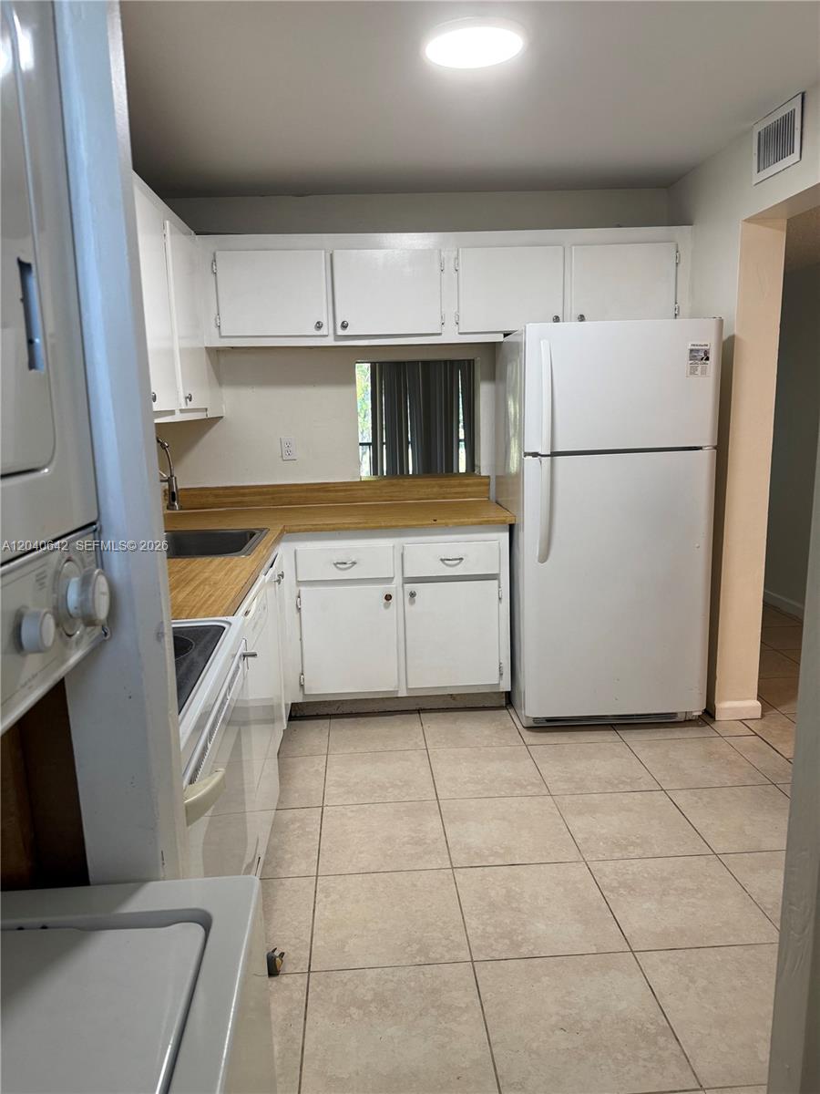 A kitchen features white cabinets, a wood-look countertop, a white refrigerator, and tiled flooring — TAMARAC, FL