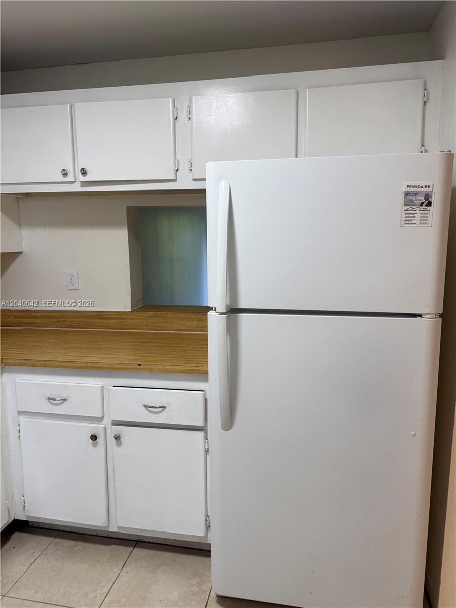 A white refrigerator stands next to white cabinets and a wood-look countertop in a kitchen — TAMARAC, FL