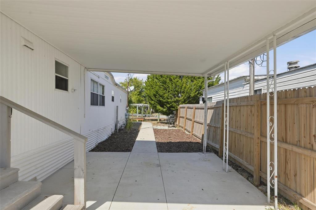 A concrete patio area sits beneath a metal carport cover beside a white mobile home — 6727 ALBATROSS LANE, HUDSON, FL