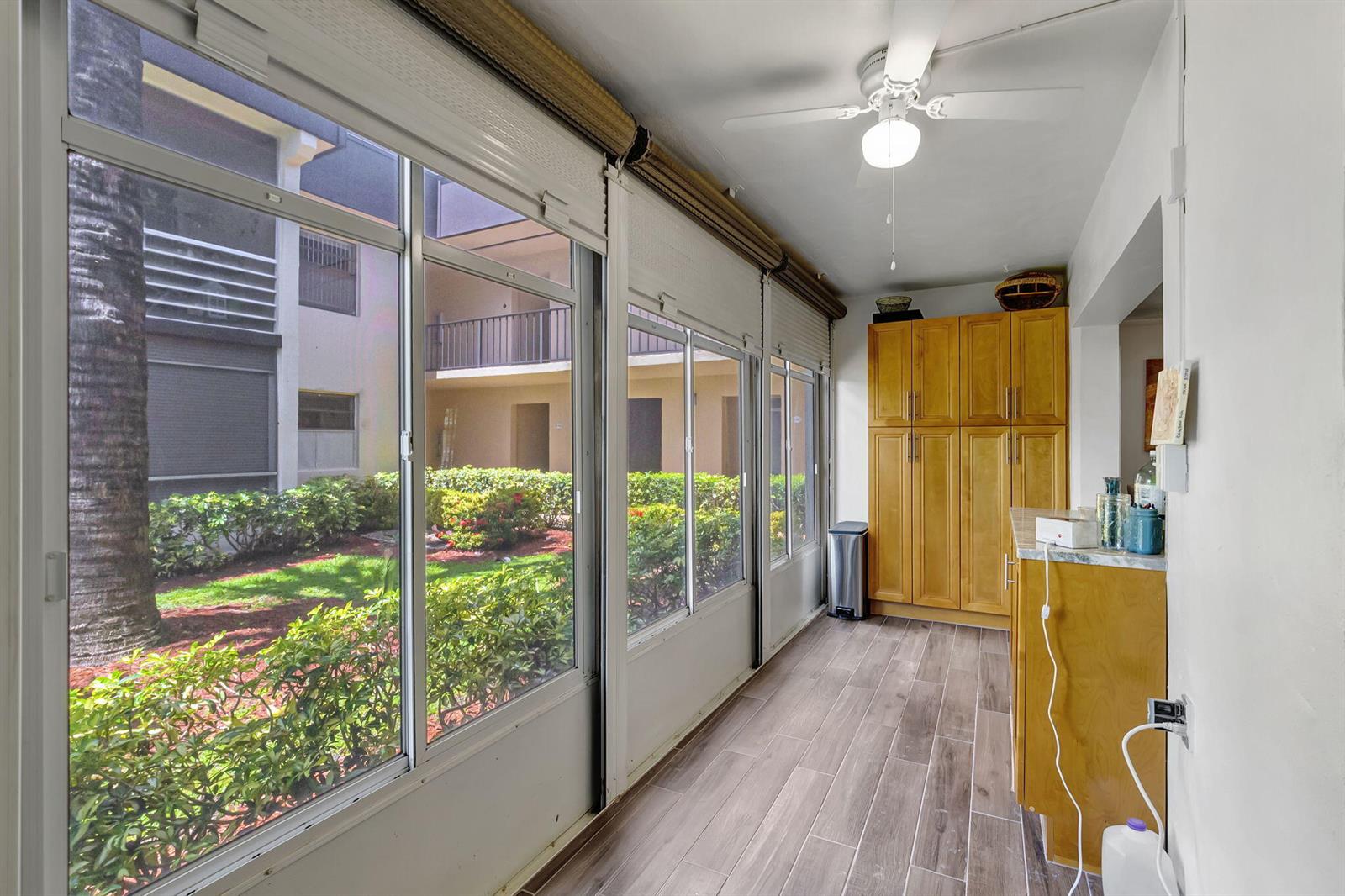 A sunroom with wood-look tile flooring, light wood cabinetry, and large windows overlooking a courtyard — 66 Capri B, Delray Beach FL 33484, DELRAY BEACH, FL