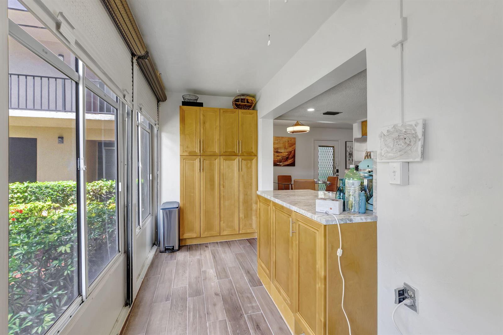A sunroom features light wood cabinetry, a marble-topped counter, and a view of outdoor greenery — 66 Capri B, Delray Beach FL 33484, DELRAY BEACH, FL