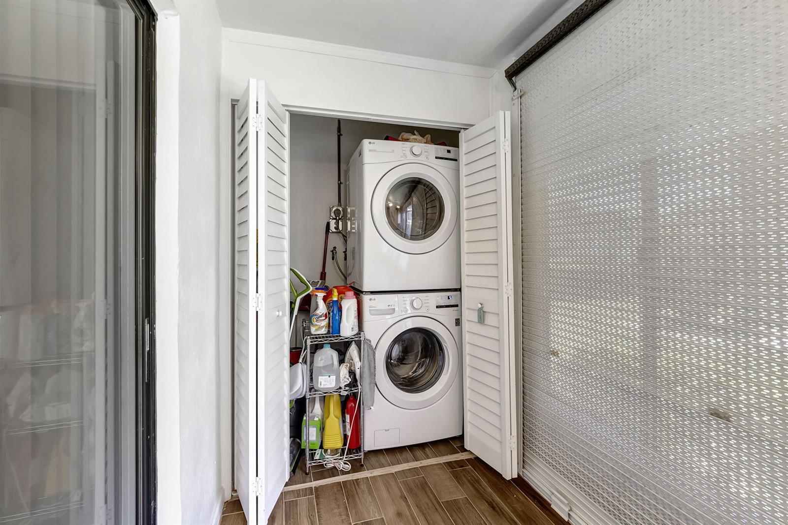 A laundry closet with a stacked washer and dryer sits beside a window with blinds — 66 Capri B, Delray Beach FL 33484, DELRAY BEACH, FL