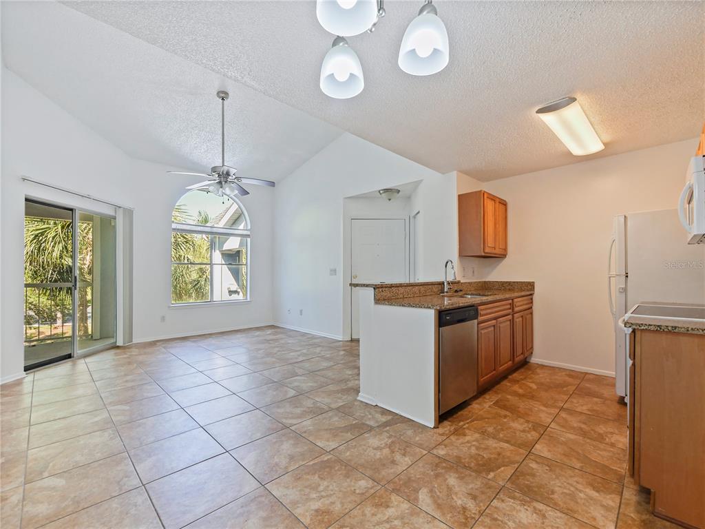 A kitchen with wood cabinets and granite countertops opens to a tiled living area — 2569 GRASSY POINT DRIVE UNIT 309, LAKE MARY, FL