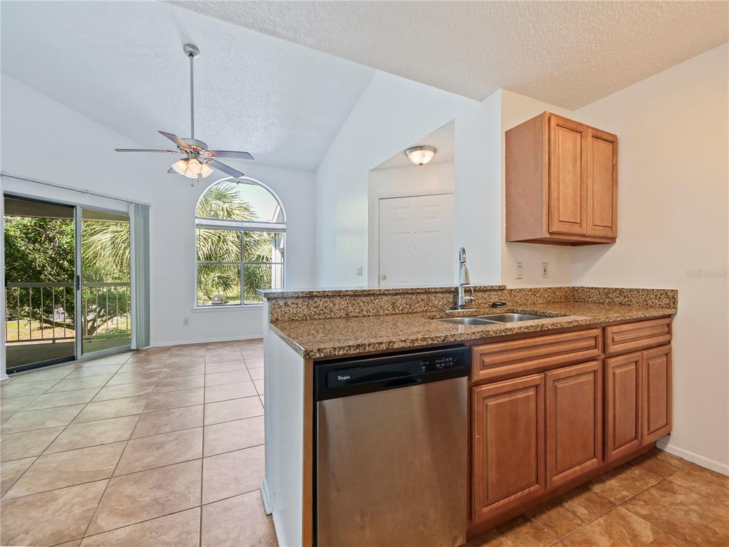 A kitchen with granite countertops and wood cabinets overlooks a living area with tile floors — 2569 GRASSY POINT DRIVE UNIT 309, LAKE MARY, FL