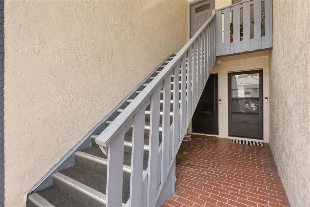 An exterior view shows a brick walkway leading to two ground-level doors and wooden stairs — 4740 AVON COURT UNIT 4740, ST CLOUD, FL